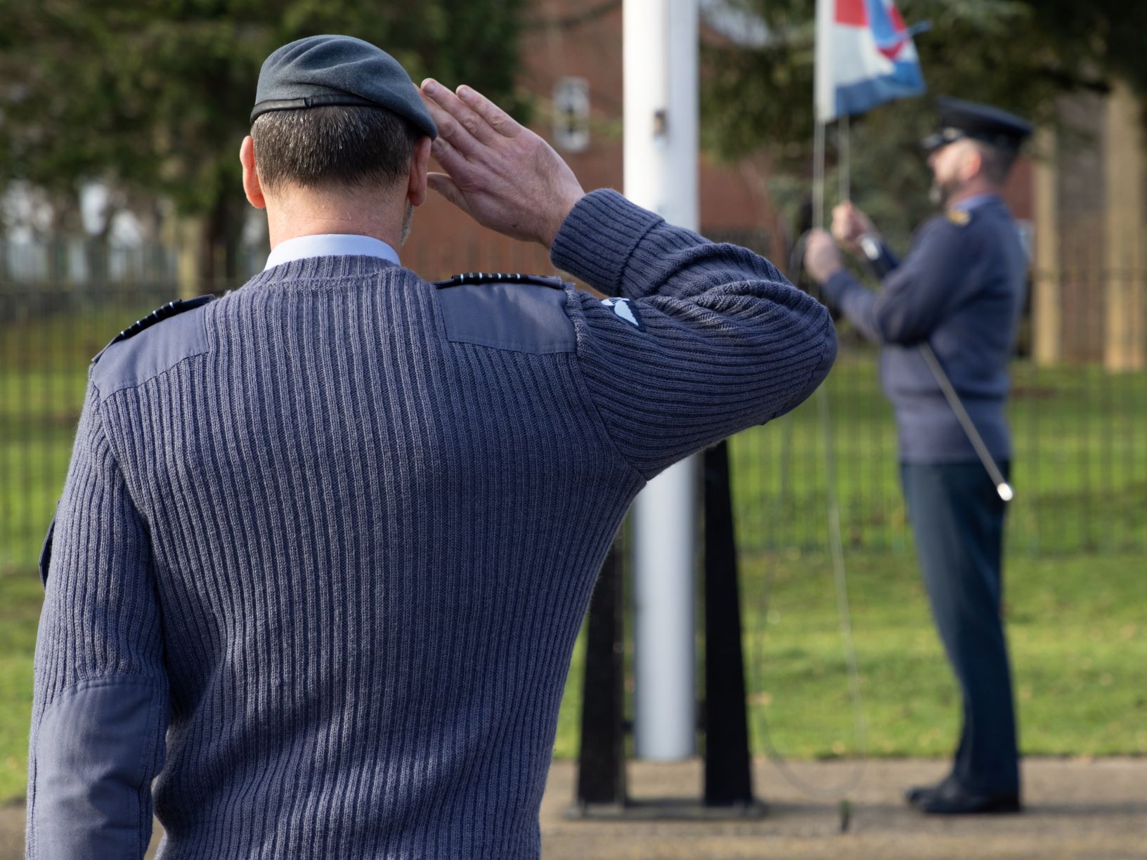 Image show Station Commander saluting a RAF aviator as he raises the flag.